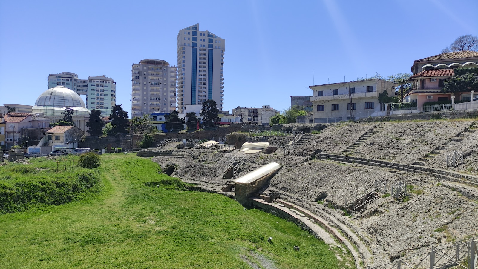 a large stone structure with a dome and a grassy area with buildings in the background